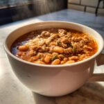 Close-up of steaming hot Spicy Turkey White Bean Chili filled with ground turkey and white beans in a white mug.