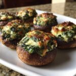 Close-up of baked Spinach and Feta Stuffed Mushrooms with golden-brown cheese topping on a white platter.