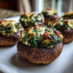 Close-up of baked Spinach and Feta Stuffed Mushrooms with golden, melted cheese topping on a white serving dish.