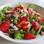 Close-up of a vibrant Spring Mix Salad with Strawberries and Goat Cheese drizzled with balsamic glaze.