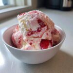 Close-up of scoops of homemade Strawberry Banana Ice Cream swirled with fresh strawberry pieces in a white bowl.