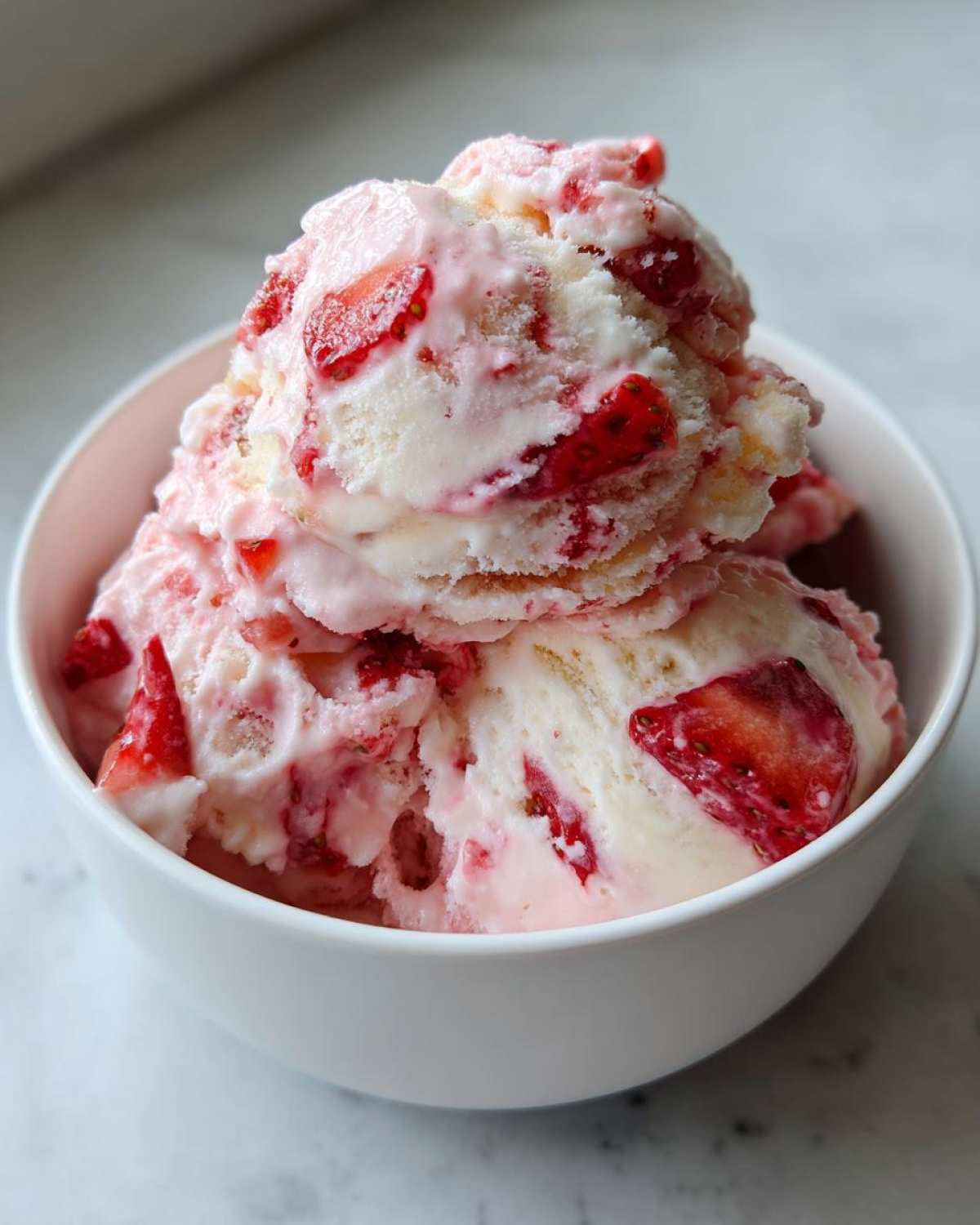 Close-up of scoops of homemade Strawberry Banana Ice Cream swirled with pink fruit chunks in a white bowl.
