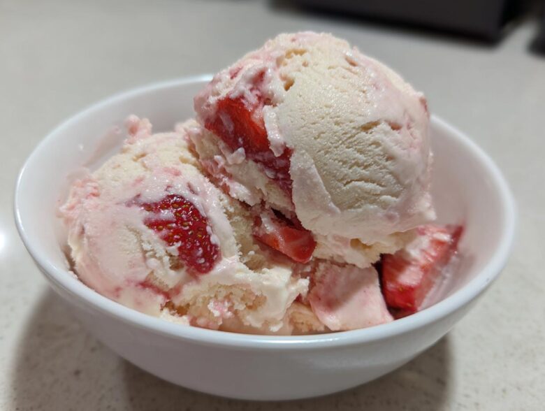 Close-up of creamy Strawberry Banana Ice Cream scoops swirled with fresh strawberry pieces in a white bowl.