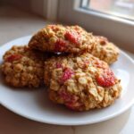 A stack of four golden Strawberry Oatmeal Breakfast Cookies featuring visible pieces of bright red strawberries on a white plate.