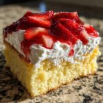 Close-up of a moist slice of Strawberry Shortcake Sheet Cake topped with thick whipped cream and glazed strawberries.