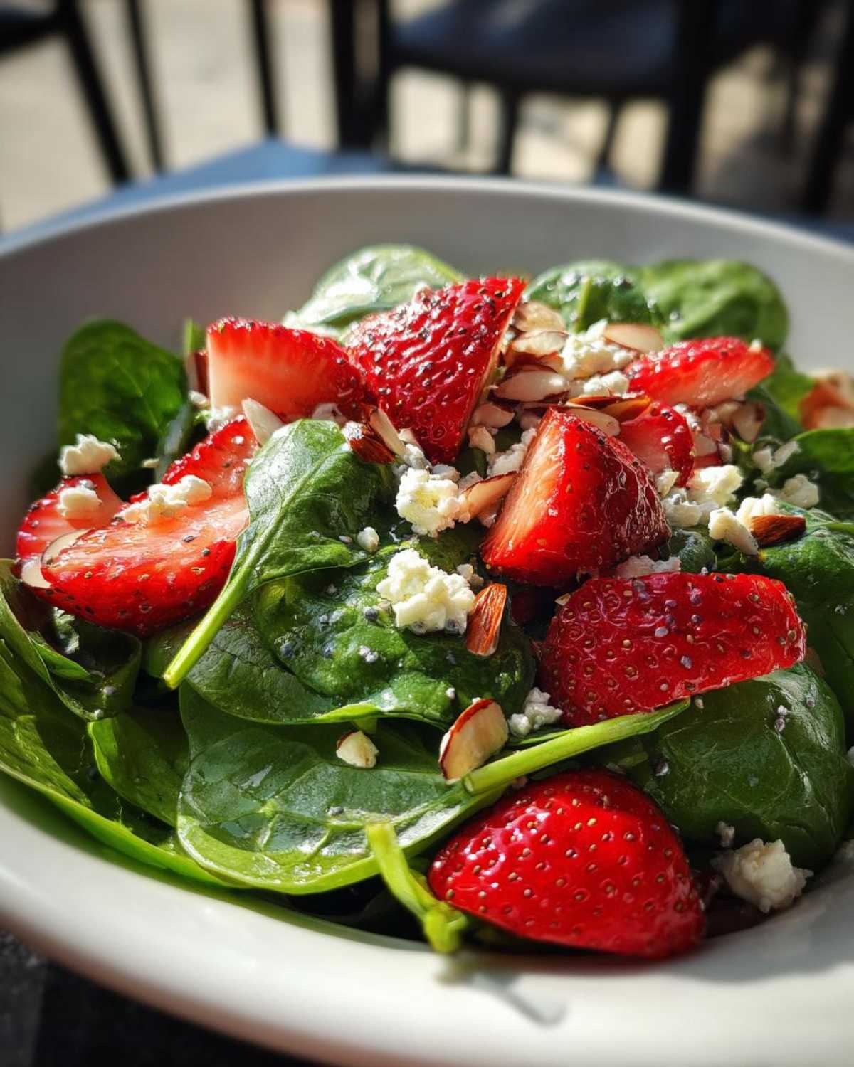 Close-up of a vibrant Strawberry Spinach Salad with poppy seeds visible on the strawberries and crumbled feta cheese.