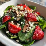 Close-up of fresh Strawberry Spinach Salad topped with feta cheese, sliced almonds, and poppy seeds.