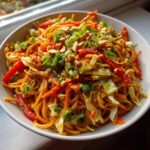Close-up of a bowl of Thai Peanut Noodles with Crunchy Veggies, topped with peanuts and green onions.