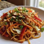 A serving of Thai Peanut Noodles with Crunchy Veggies, topped with chopped peanuts and green onions.