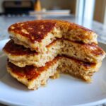 Close-up of a stack of three fluffy Vegan Banana Oat Pancakes with a bite taken out, showing the moist oat texture.