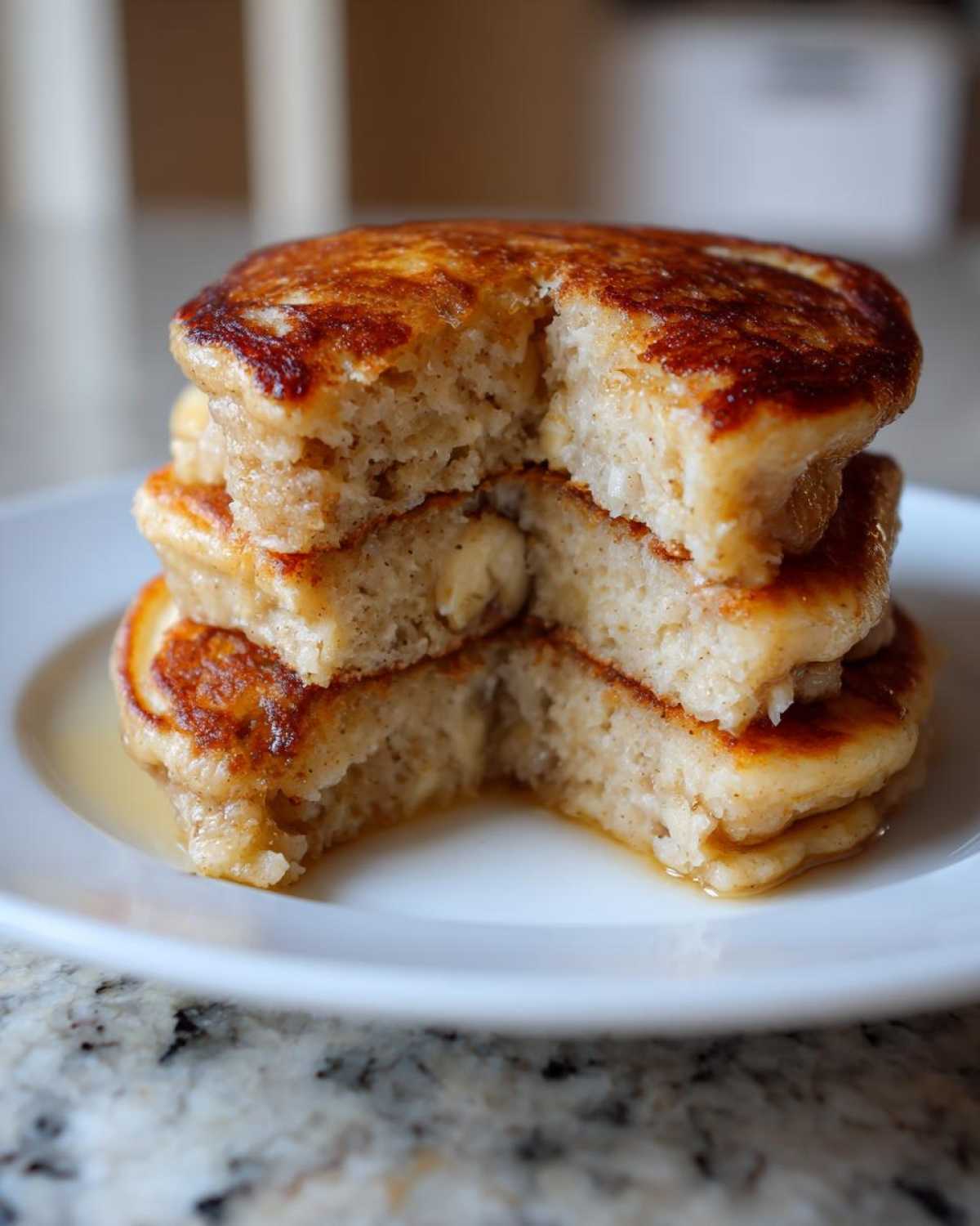 Close-up of a stack of fluffy Vegan Banana Oat Pancakes with a bite removed, showing the soft interior and syrup.