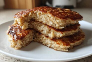 A stack of three thick Vegan Banana Oat Pancakes, cut open to show the texture of oats inside, served on a white plate.