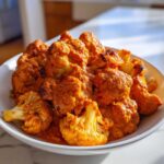 Close-up of roasted cauliflower florets coated in a vibrant orange sauce, ready to eat Vegan Cauliflower Tikka Masala.