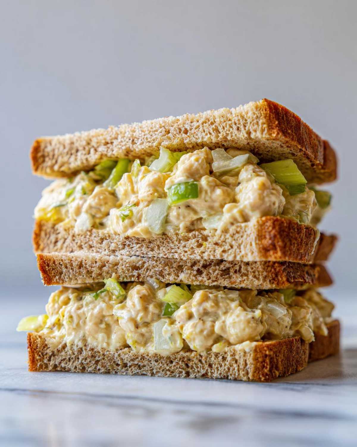 A tall stack of two halves of a Vegan Chickpea Salad Sandwich made with whole wheat bread and creamy filling.
