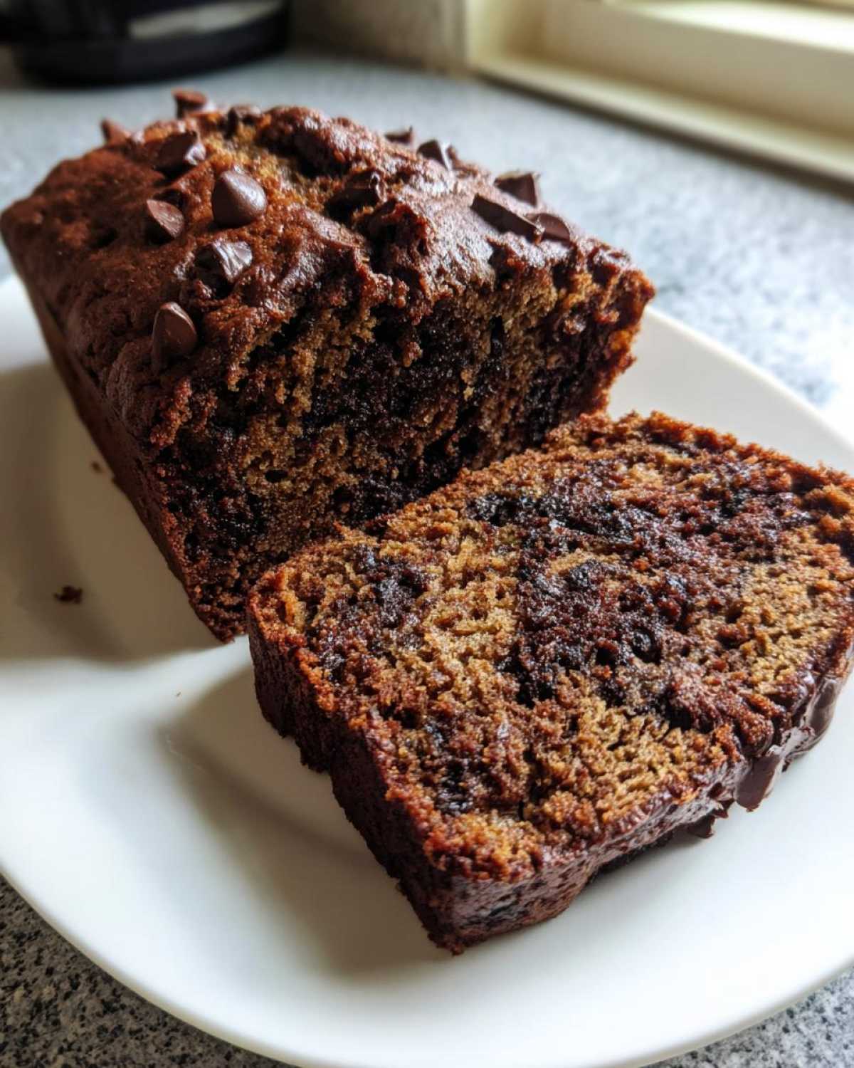 A loaf of moist Vegan Chocolate Banana Bread, partially sliced, showing rich chocolate swirls and chips on top.