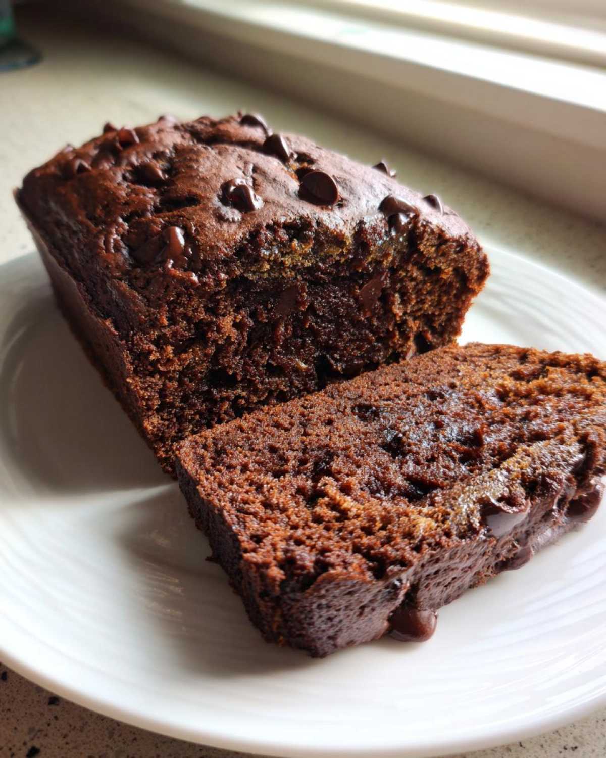 Close-up of a moist slice of Vegan Chocolate Banana Bread topped with melted chocolate chips.