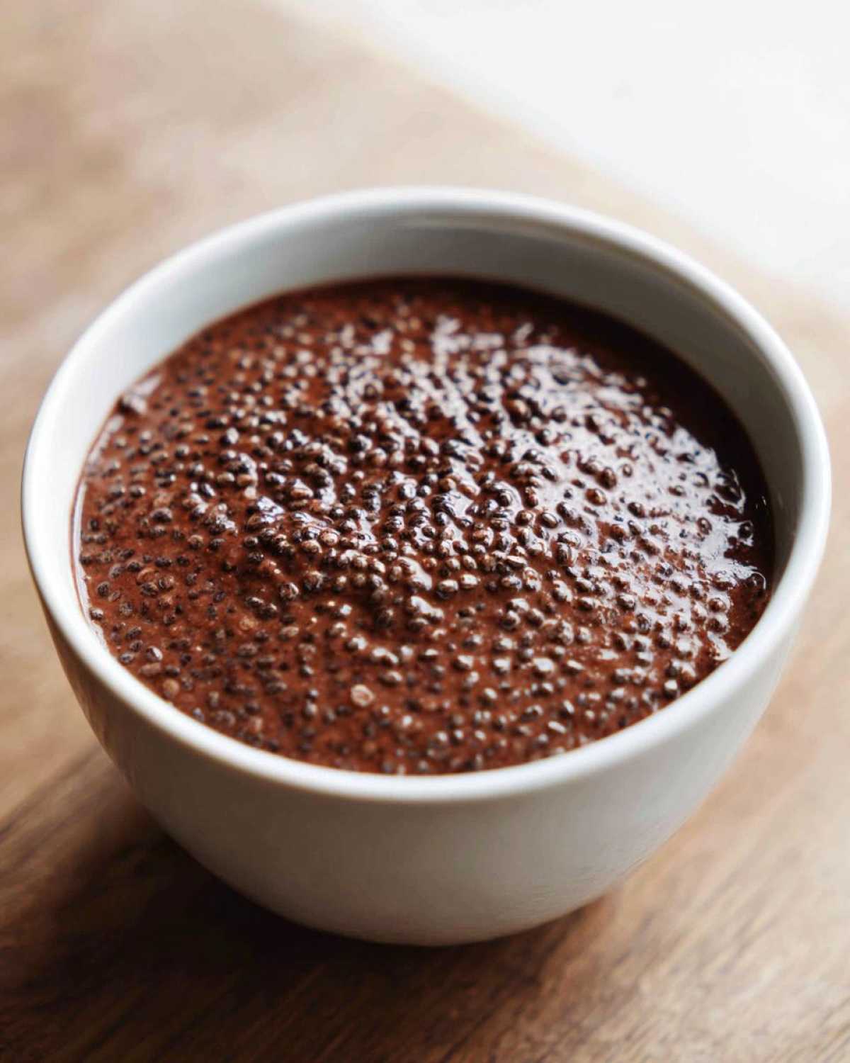 Close-up of thick, rich Vegan Chocolate Chia Pudding texture in a white bowl on a wooden surface.
