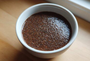 Overhead close-up of thick Vegan Chocolate Chia Pudding in a small white bowl on a wooden surface.