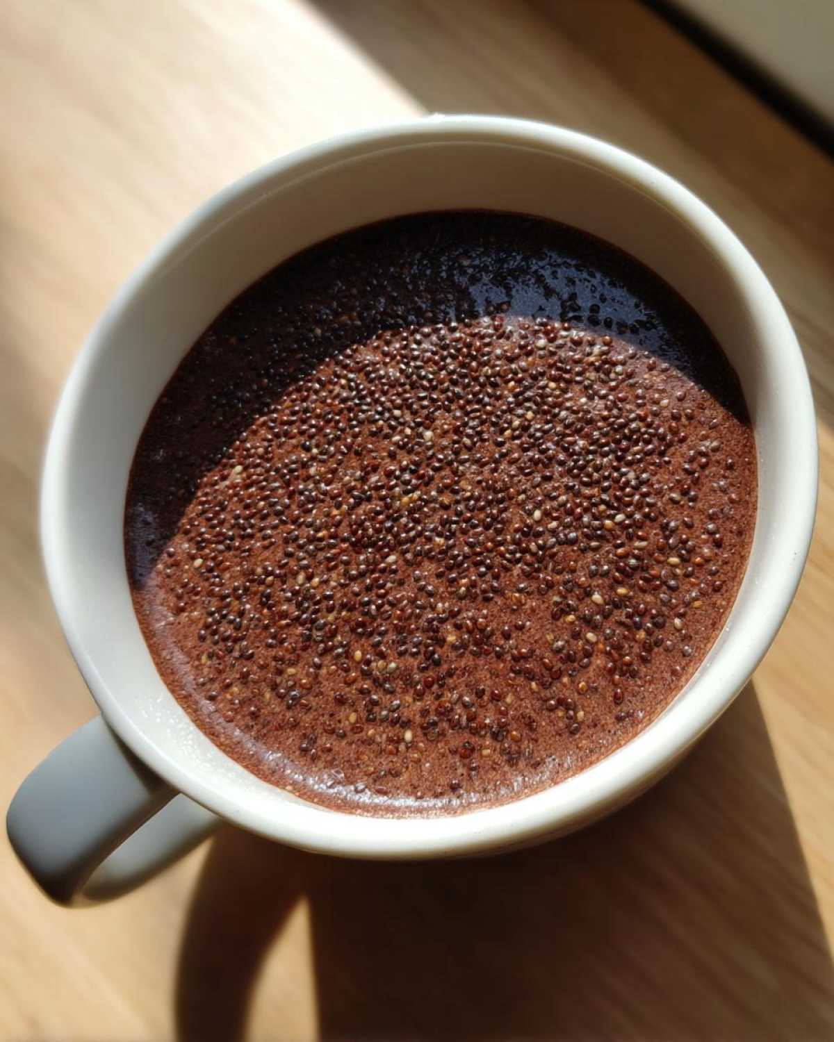 Overhead view of rich Vegan Chocolate Chia Pudding topped with visible chia seeds in a white mug.