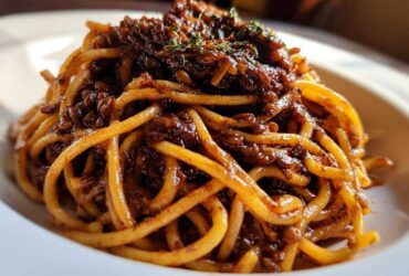 Close-up of thick spaghetti noodles coated in a rich, dark Vegan Lentil Bolognese sauce, garnished with herbs.