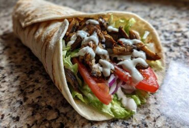 A delicious Vegan Mushroom Shawarma wrap filled with seasoned mushrooms, lettuce, tomato, onion, and drizzled with white sauce.