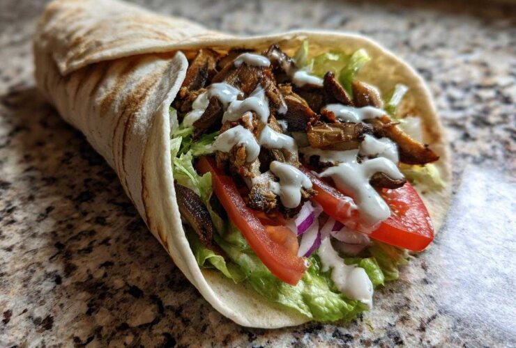 A delicious Vegan Mushroom Shawarma wrap filled with seasoned mushrooms, lettuce, tomato, onion, and drizzled with white sauce.