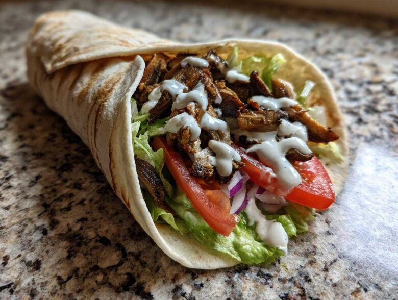 A delicious Vegan Mushroom Shawarma wrap filled with seasoned mushrooms, lettuce, tomato, onion, and drizzled with white sauce.