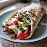 A close-up of a freshly made Vegan Mushroom Shawarma wrap drizzled with white sauce on a light blue plate.