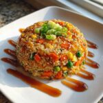 A molded serving of Vegetable Fried Rice with Sesame Ginger Sauce, topped with scallions and sesame seeds.