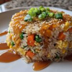 A molded serving of Vegetable Fried Rice with Sesame Ginger Sauce, topped with green onions and sesame seeds.