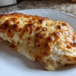 A close-up of a single serving of Cheesy Baked Chicken with Cream Sauce, topped with bubbly, browned cheese.