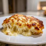A close-up of a serving of Cheesy Baked Chicken with Cream Sauce, featuring a thick layer of golden-brown melted cheese.
