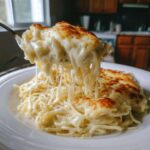 A fork lifting a portion of Cheesy Chicken Alfredo Bake, showing long, stretchy cheese pulls over the creamy pasta.