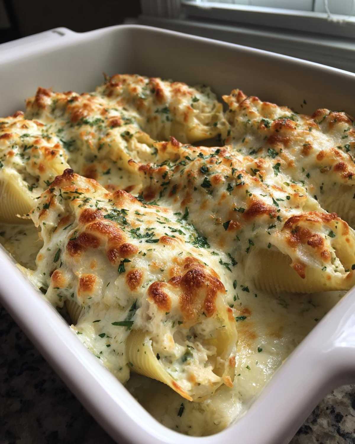 Close-up of baked Cheesy Chicken Alfredo Stuffed Pasta Shells topped with melted, browned cheese and parsley.