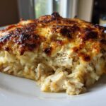 A close-up serving of Cheesy Chicken and Rice Bake with Golden Top, showing shredded chicken and rice under a browned, bubbly cheese crust.