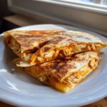 Three wedges of perfectly golden and crispy Cheesy Chicken Quesadilla stacked on a white plate.