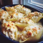 Close-up of baked Cheesy Chicken Stuffed Pasta shells topped with melted, browned cheese in a creamy sauce.