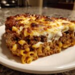 A thick, square slice of Cheesy Ground Beef Pasta Bake Comfort Food with a browned, bubbly cheese topping.
