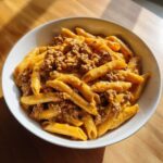 A white bowl filled with Cheesy Ground Beef Pasta with Creamy Sauce, featuring penne pasta coated in orange sauce and ground meat.