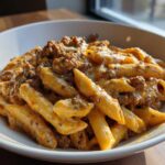 A white bowl filled with Cheesy Ground Beef Pasta with Creamy Sauce, featuring penne pasta coated in a rich, orange-hued sauce and ground beef.