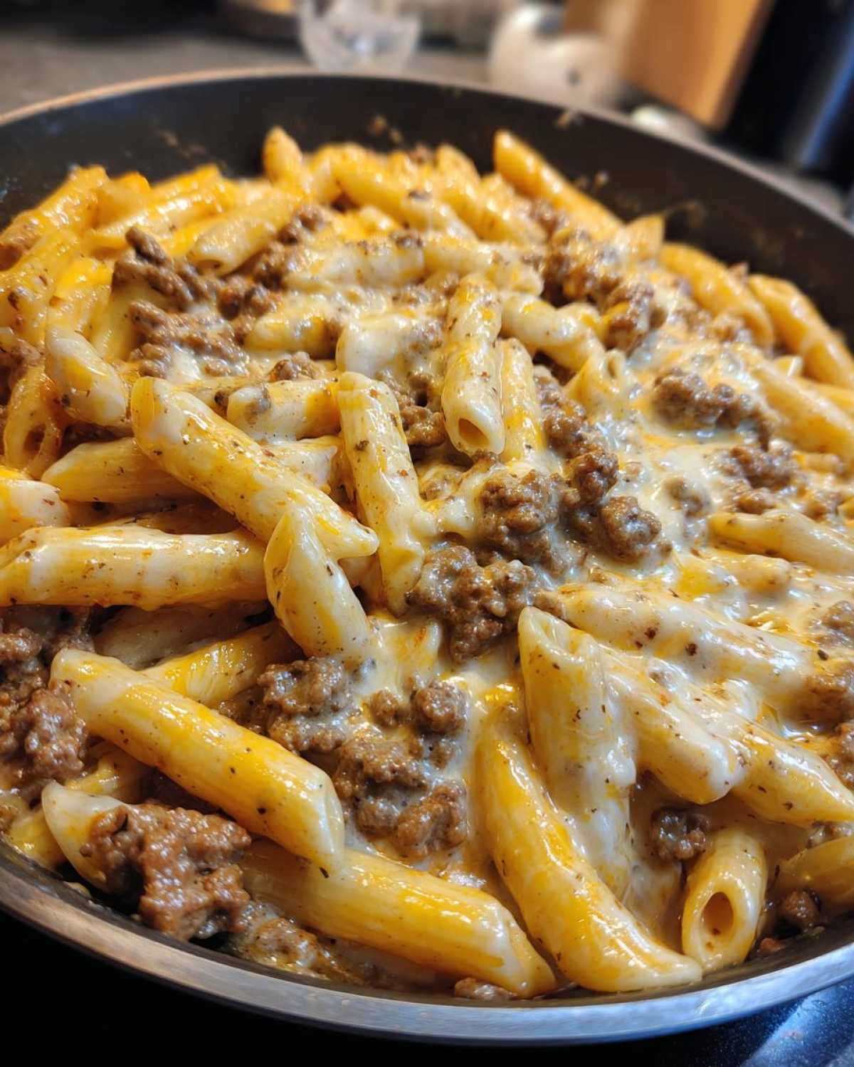 Close-up of Cheesy Ground Beef Pasta Skillet with penne pasta, ground beef, and melted cheese sauce in a black skillet.