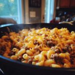 Close-up of steaming Cheesy Ground Beef Pasta Skillet Comfort Food topped with melted cheddar cheese in a black pan.