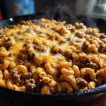 Close-up of steaming Cheesy Ground Beef Pasta Skillet Comfort Food topped with melted cheddar cheese.