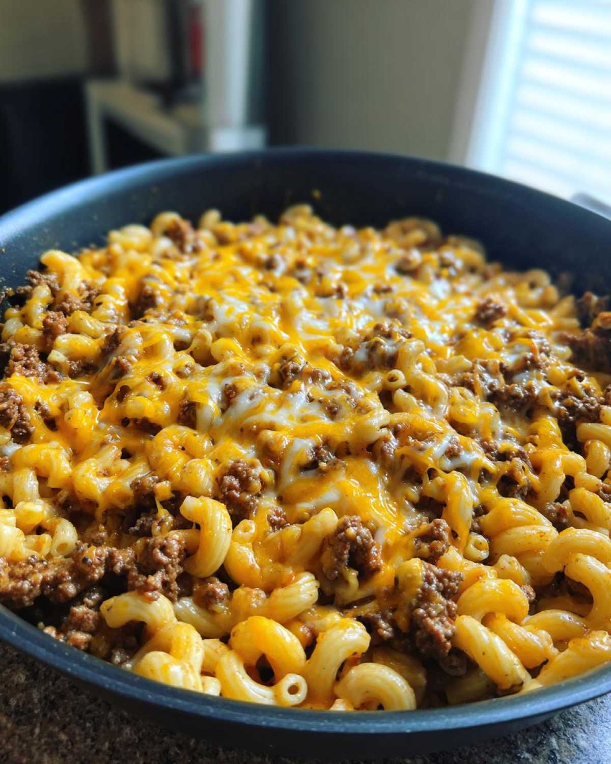 Close-up of Cheesy Ground Beef Pasta Skillet Comfort Food with melted cheddar and mozzarella in a black skillet.