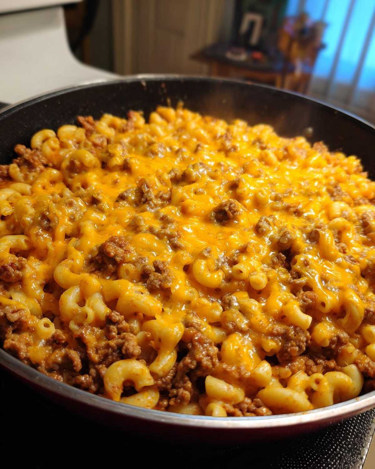 Close-up of Cheesy Ground Beef Pasta Skillet Comfort Food topped with melted cheddar cheese in a black skillet.