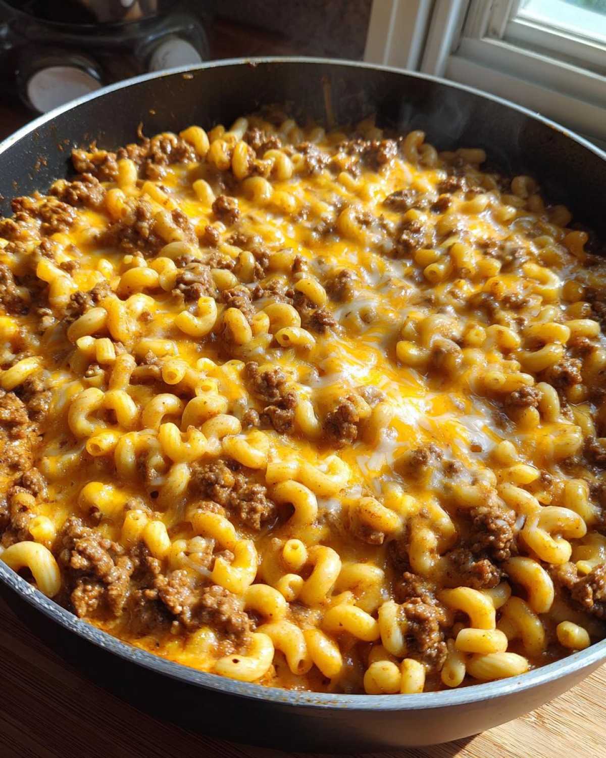 Close-up of Cheesy Ground Beef Pasta Skillet Comfort Food with melted cheddar cheese topping in a black skillet.