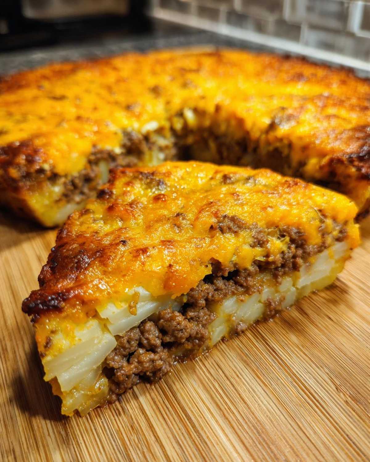 A thick slice of Cheesy Ground Beef and Potato Bake Comfort Food featuring layers of potatoes, seasoned ground beef, and a melted, browned cheese topping.