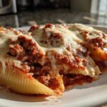 Close-up of three Cheesy Ground Beef Stuffed Shells with Cream Sauce covered in melted mozzarella cheese on a white plate.