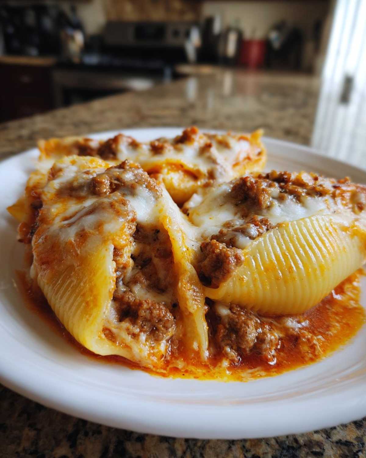 Close-up of baked Cheesy Ground Beef Stuffed Shells with cream sauce and melted mozzarella cheese on a white plate.
