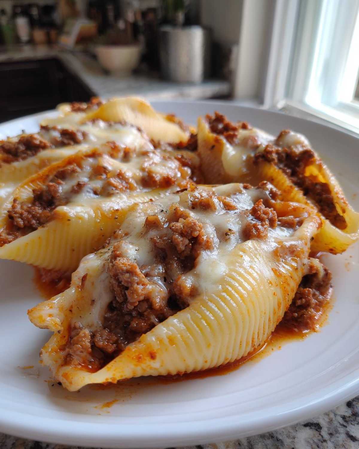 Close-up of baked Cheesy Ground Beef Stuffed Shells with melted mozzarella cheese on a white plate.